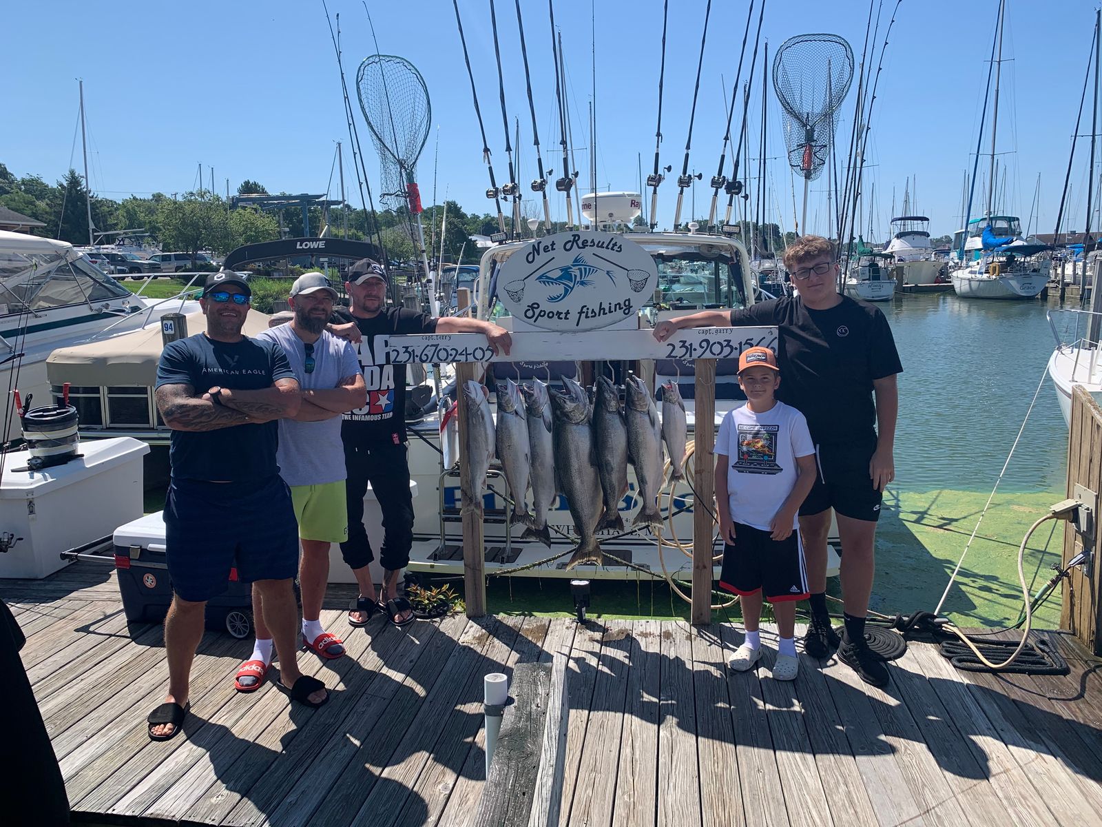 A charter group on the marina dock with a large catch of fish laid out, the Net Results Sport Fishing boat behind them