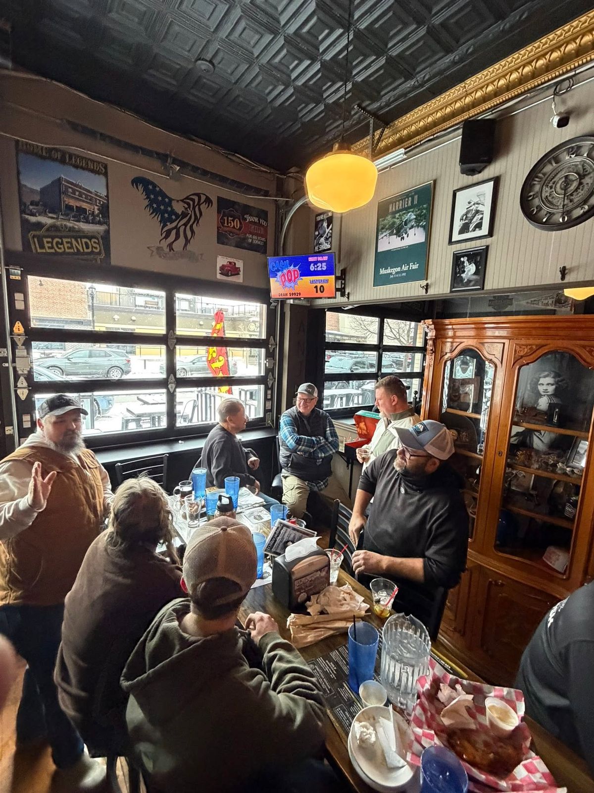 A rustic fishing-themed gathering space with patrons around tables, vintage nautical décor and memorabilia on the walls