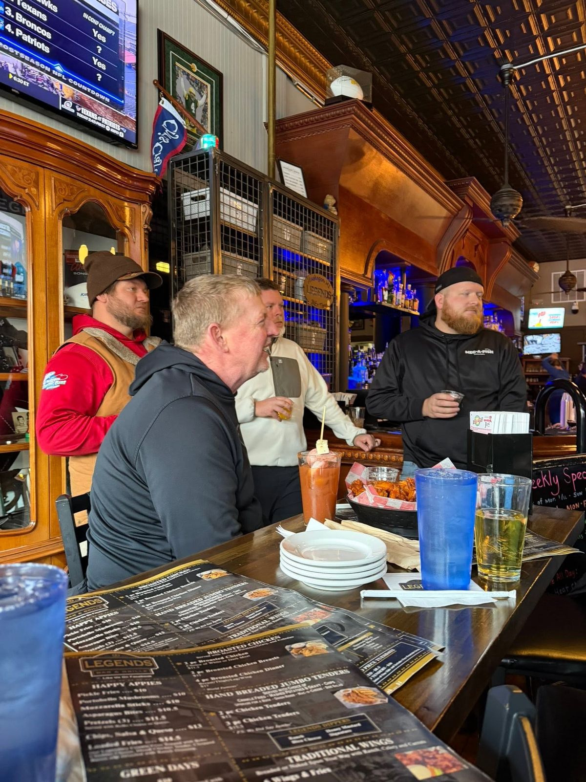 Men gathered at the bar of a wooden-interior restaurant, menus on the counter
