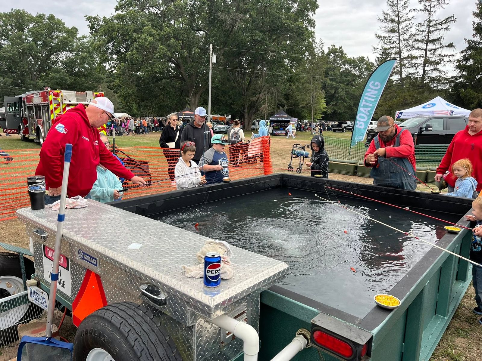 Association members and volunteers in red jackets running a children's fishing demonstration with portable tanks at an outdoor community event