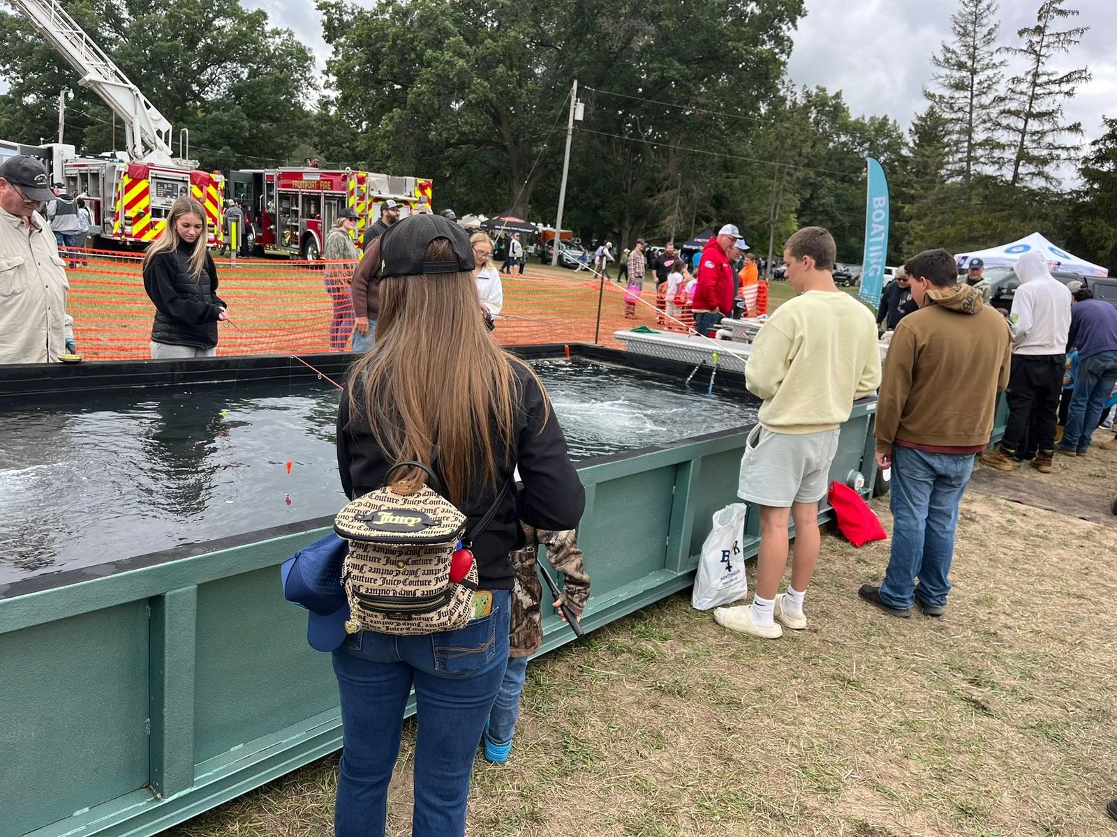 A large outdoor fishing tank with participants and spectators, fire trucks and vendor tents behind