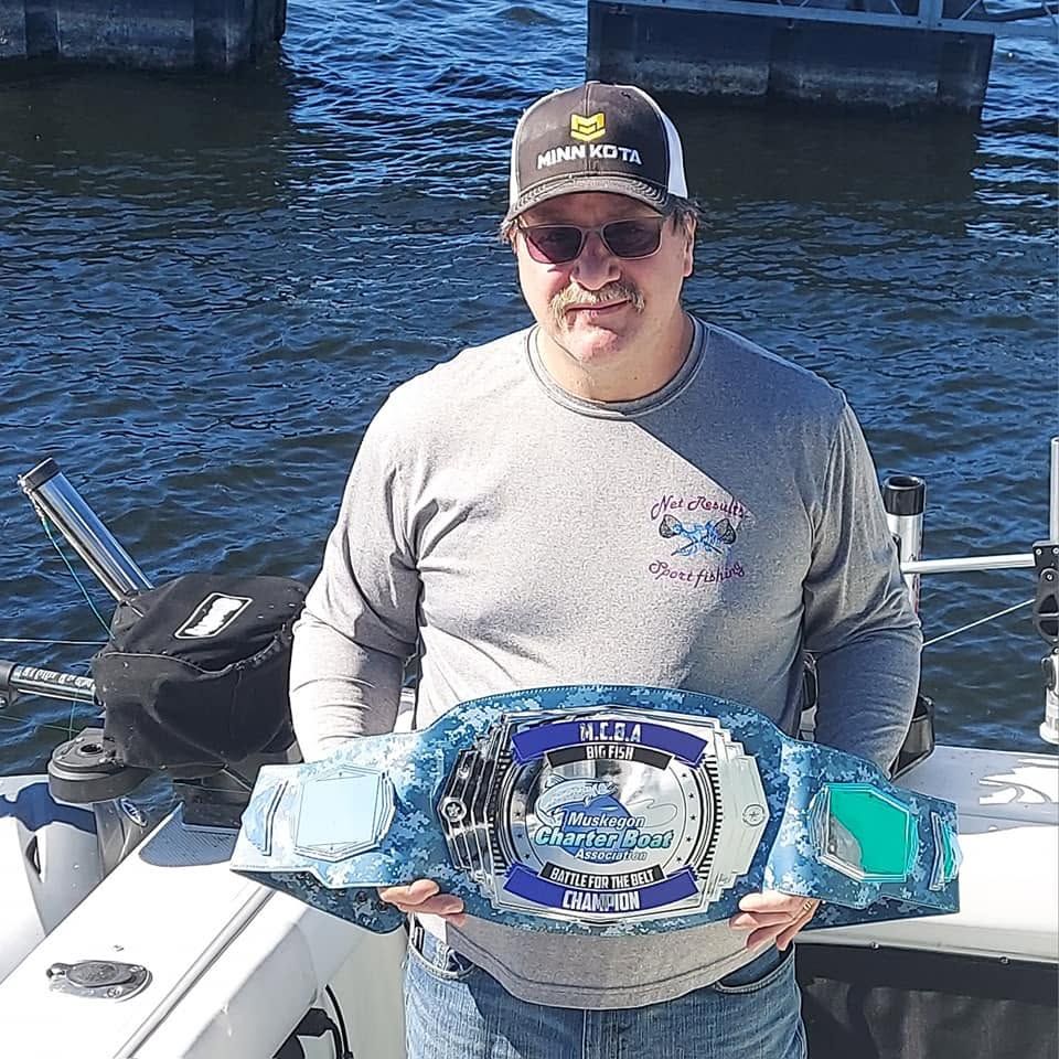 A charter captain aboard his boat in Muskegon waters holding up the MCBA big fish belt