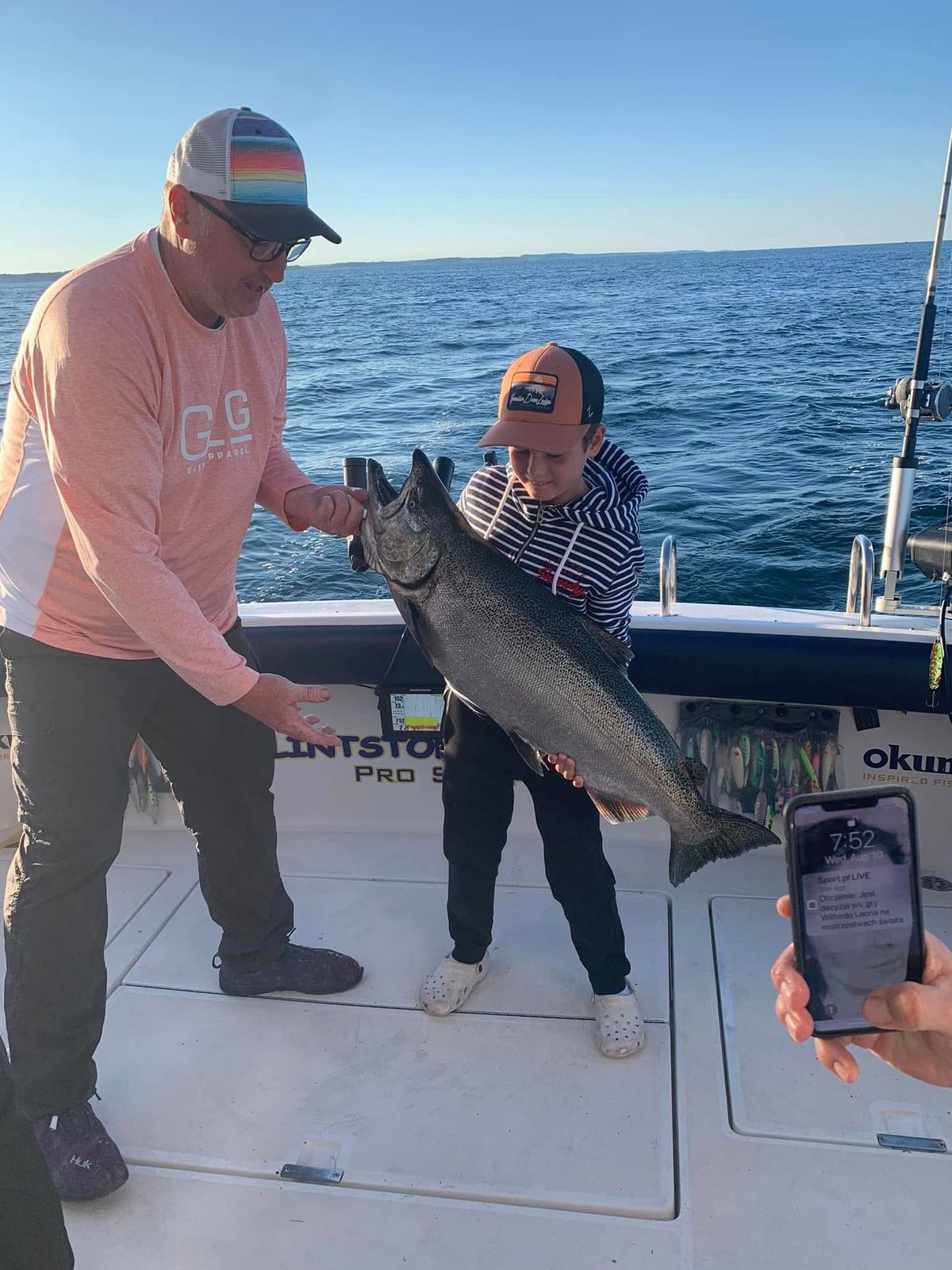 A young angler holding up a large lake trout beside the captain on a Muskegon charter boat