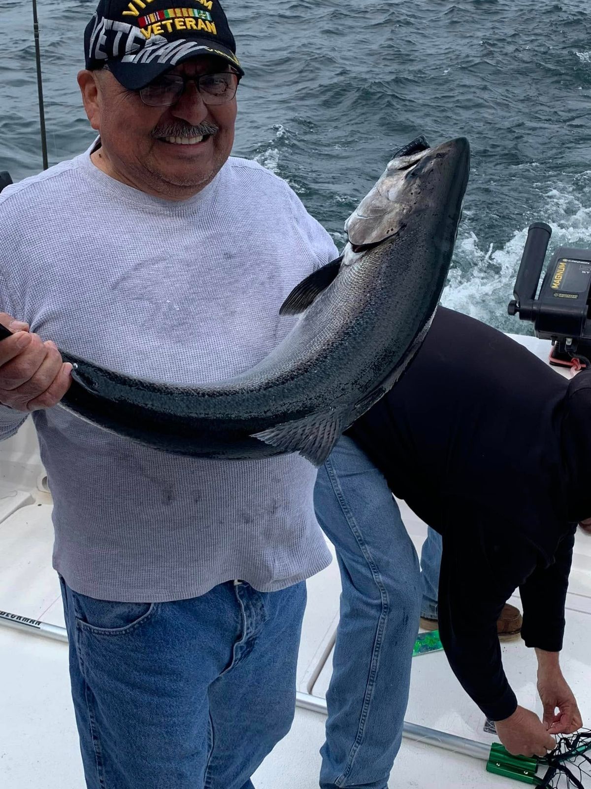 A recreational fisherman holding a large lake trout aboard a charter boat on Lake Michigan