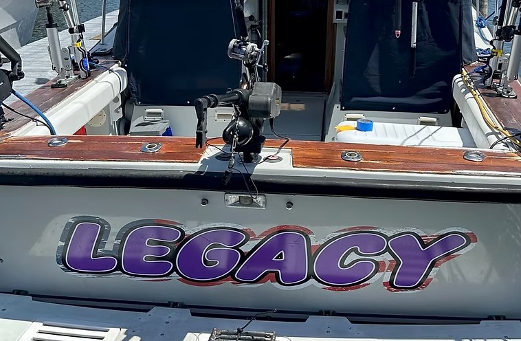 Legacy's transom at the dock, the name in purple over the teak covering board
