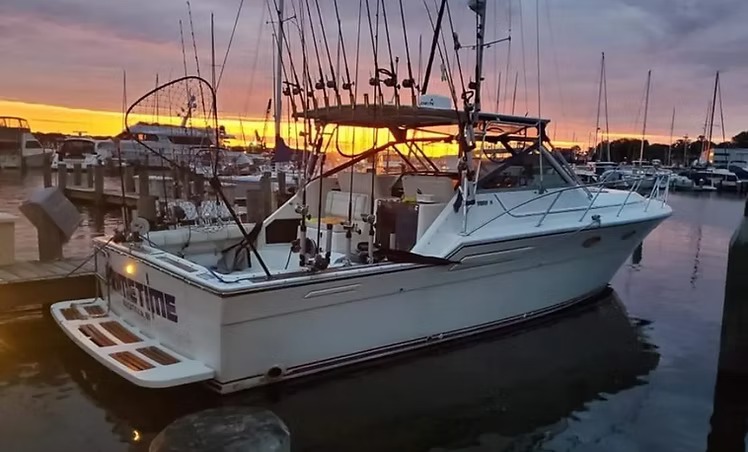 A charter boat moored stern to the dock at sunset, rods racked and the sky burning orange behind the marina
