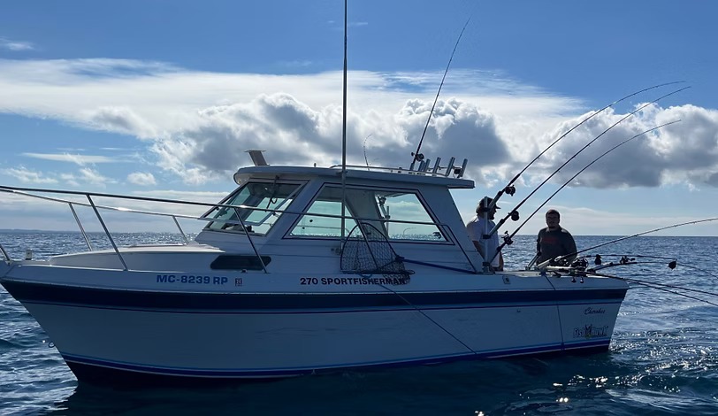 A 270 Sportfisherman running offshore under a bank of cloud, two anglers working the rods aft