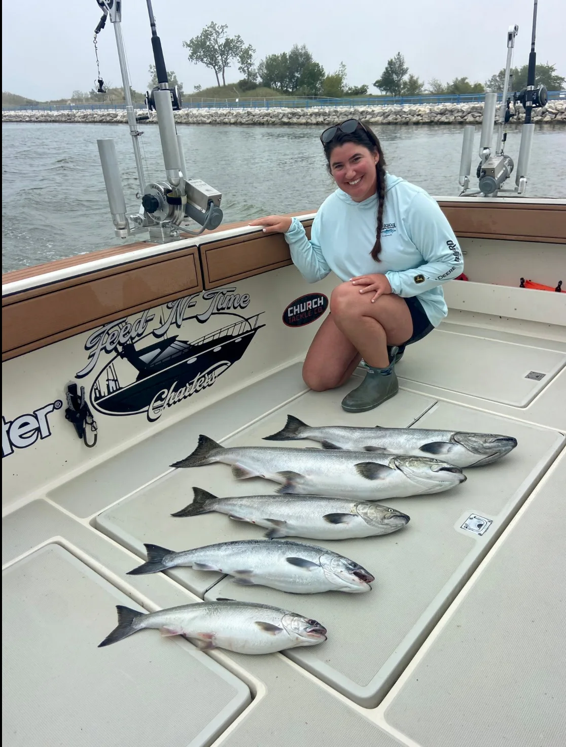 An angler kneeling on the deck of a charter boat beside five freshly caught salmon laid out on the deck
