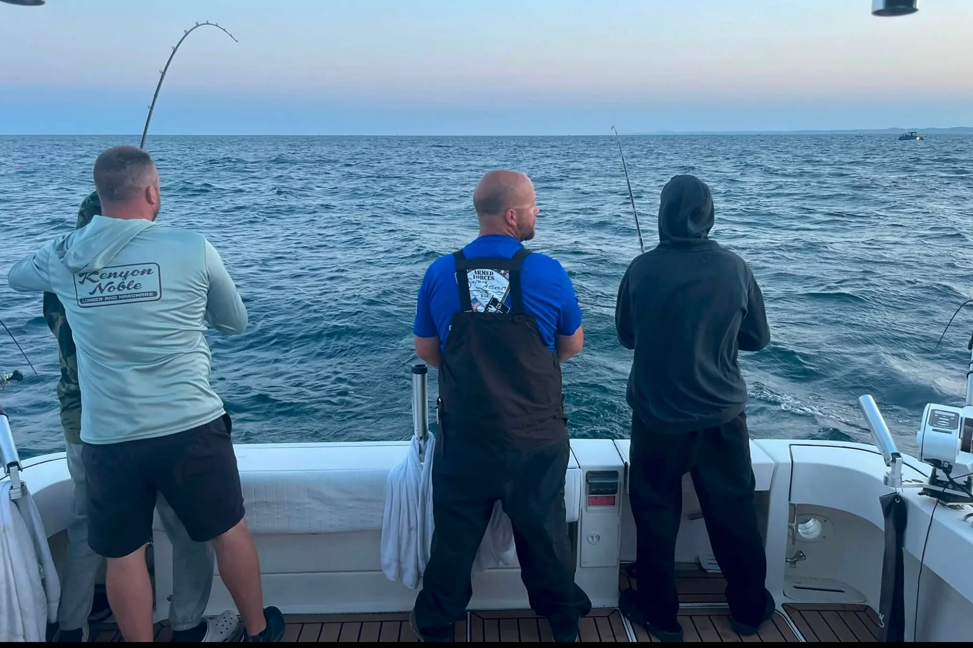 Three anglers working bent rods off the stern of a charter boat on Lake Michigan at dusk