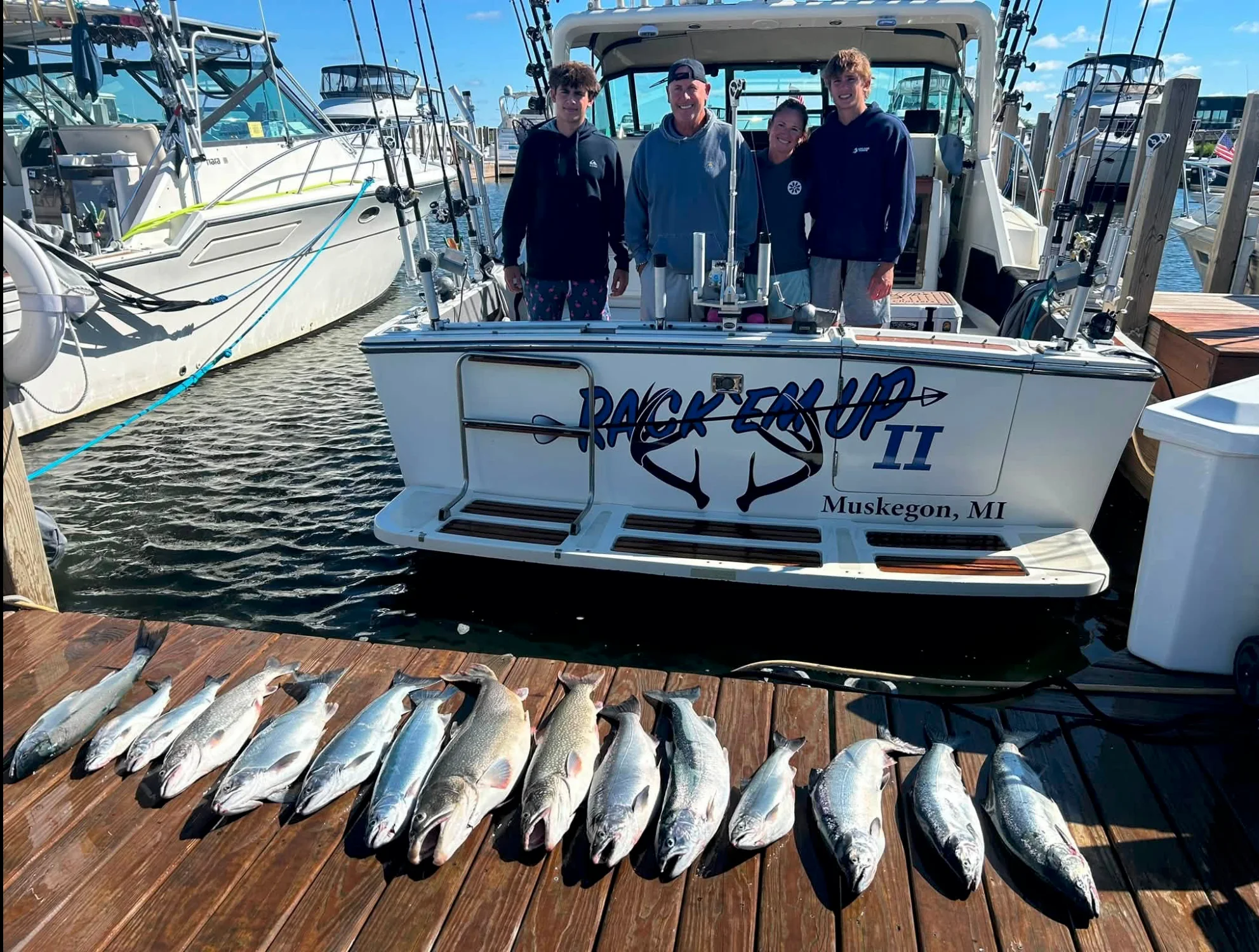 A family of four standing on the stern of the charter boat Rack 'Em Up II at the Muskegon marina, with a long row of salmon and lake trout laid out on the dock